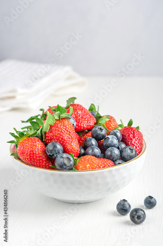 Fresh organic red garden strawberries and blueberries with characteristic aroma  juicy texture  and sweetness  source of vitamin C and dietary minerals served in bowl on white wooden table. Vertical
