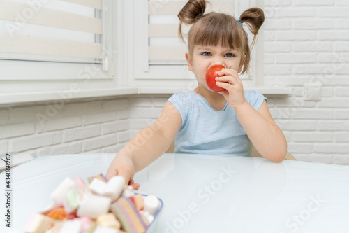 the girl eats a delicious ripe tomato and reaches for unhealthy sweets. healthy food selection concept