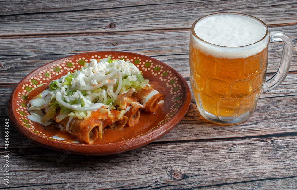 hero, side view, horizontal potato and beef fried tacos, in a Mexican mud plate with cream lettuce tomato salsa and onions with lemon on top with a jar of cold beer on the side. Tacos dorados concept. hero, side view, horizontal potato and beef fried tacos, in a Mexican mud plate with cream lettuce tomato salsa and onions with lemon on top with a jar of cold beer on the side. Tacos dorados concept.
