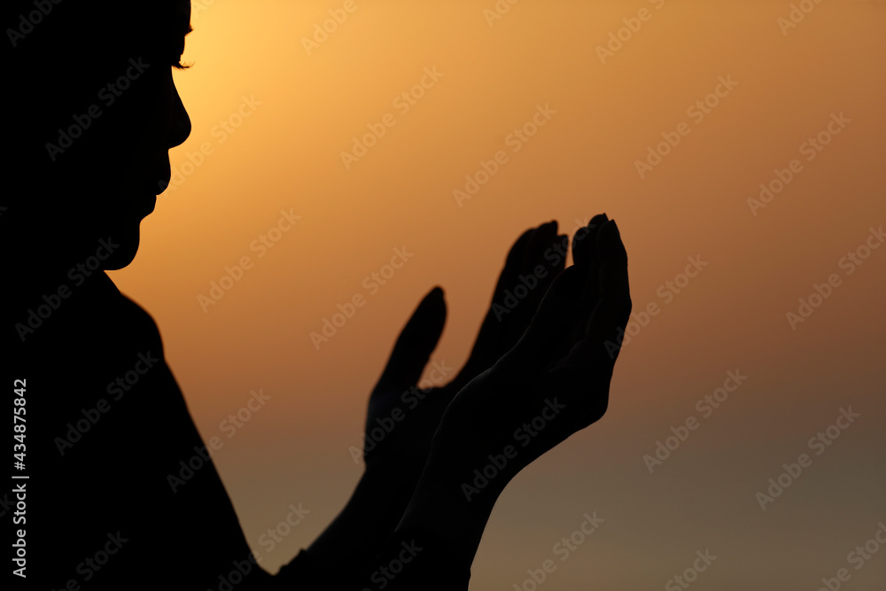 Silhouette of muslim woman in abaya praying with her hands up in air at sunset. Religion praying concept. . United Arab Emirates