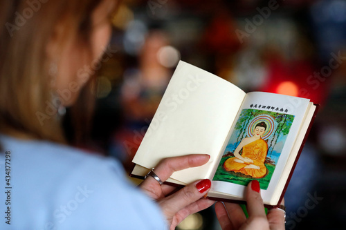 Thien Minh buddhist temple.  Woman reading sacred buddhist texts.  Shakyamuni Buddha illustration on the first page.  France.