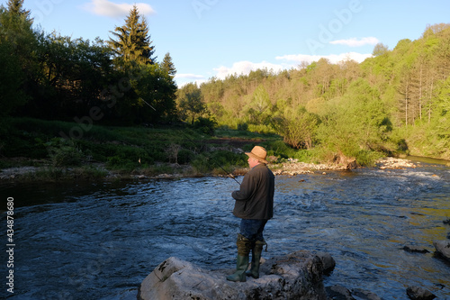 Senior man with a hat fishing in the mountain river on a fishing lure