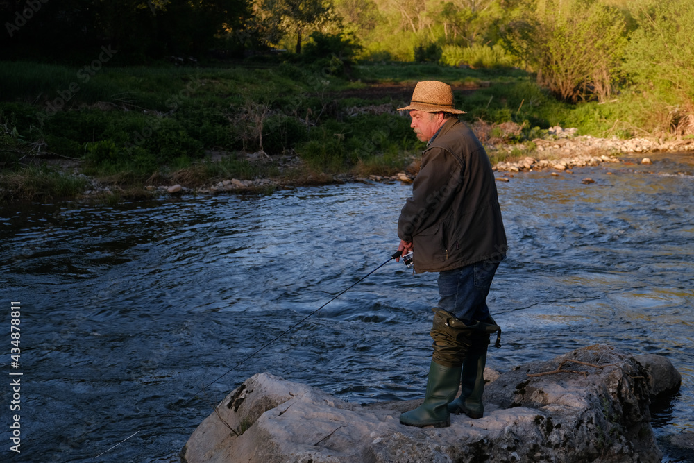 Senior man with a hat fishing in the mountain river on a fishing lure Senior man with a hat fishing in the mountain river on a fishing lure
