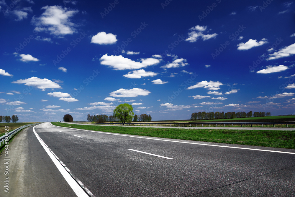 A long highway stretches into the distance under a blue sky and white clouds