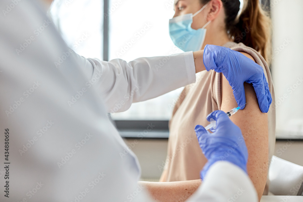 Fototapeta premium health, medicine and pandemic concept - female doctor or nurse wearing protective medical mask with syringe vaccinating patient at hospital