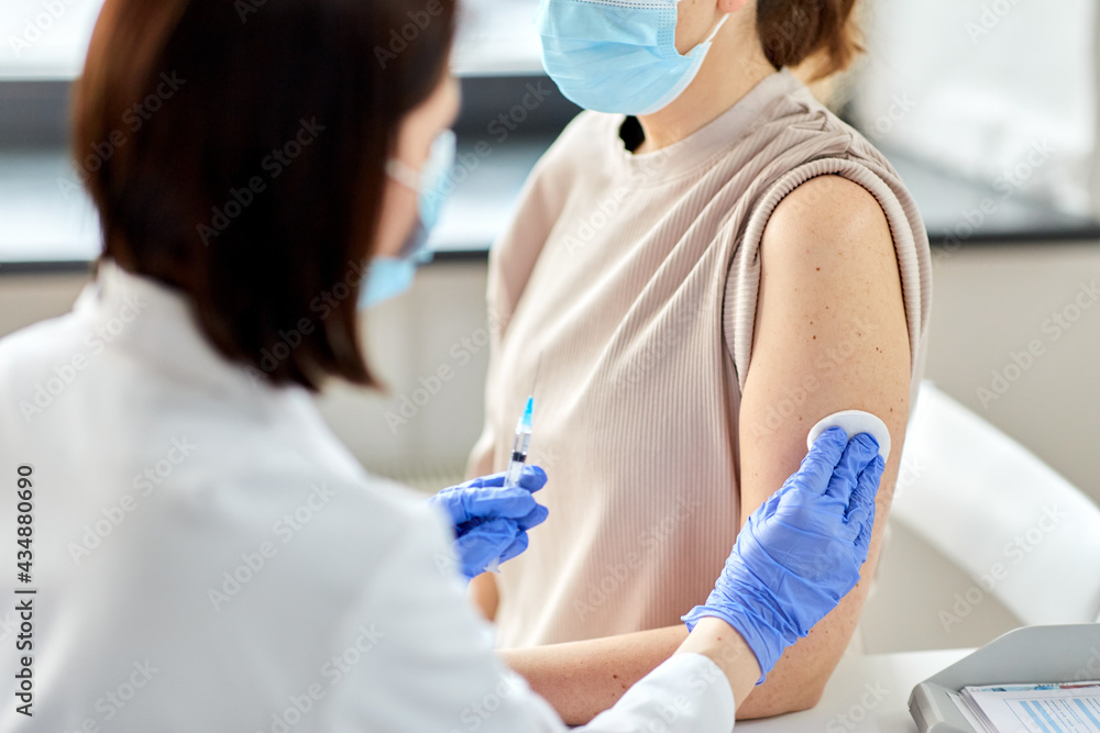 Fototapeta premium health, medicine and pandemic concept - close up of female doctor or nurse wearing protective medical gloves with syringe vaccinating patient at hospital
