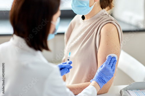 health, medicine and pandemic concept - close up of female doctor or nurse wearing protective medical gloves with syringe vaccinating patient at hospital