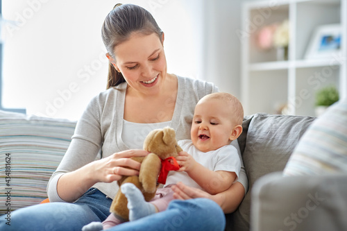 family, motherhood and people concept - happy smiling mother and little baby playing with teddy bear toy at home
