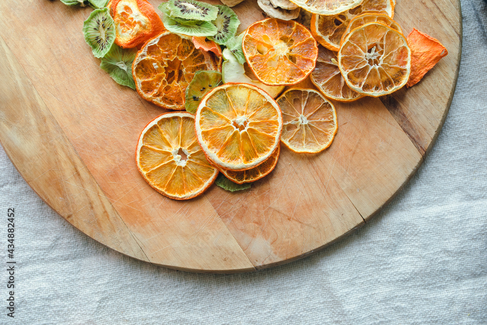 Part view of a round wooden board with dried fruits like orange, kiwi, apple, tangerine on a background of linnen fablic. Part view of a round wooden board with dried fruits like orange, kiwi, apple, tangerine on a background of linnen fablic.