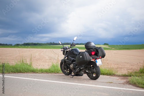 naked unrecognizable black motorcycle with suitcases on the sides stands on the side of the harvested field