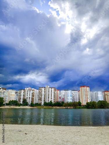 Scenic beautiful cityscape with urban pond  lake near residential district with new buildings against bright blue sky before storm  rain  thunder