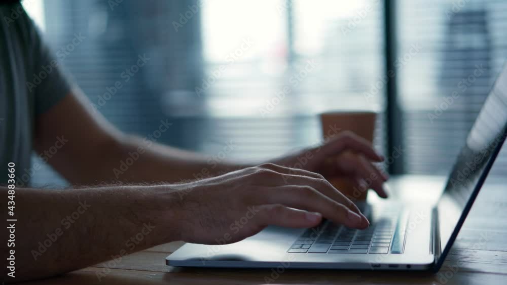 Close-up real-time side footage of man's hands typing on a laptop keyboard.