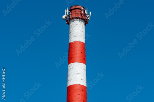 A large industrial smokestack against a blue sky. Red and white pipe in commercial enterprises or power plants.