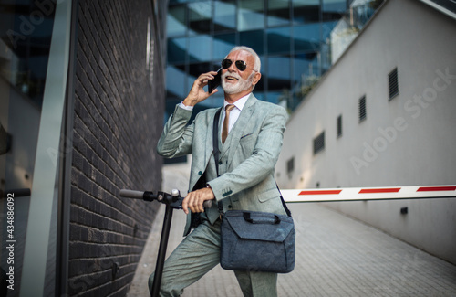 Senior business man with electric scooter in the city. Using smart phone.