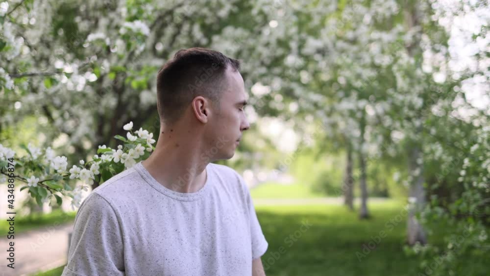 A young man of European appearance stands among the trees of flowering apple trees. The flowering period is in May. A young man of European appearance stands among the trees of flowering apple trees. The flowering period is in May.