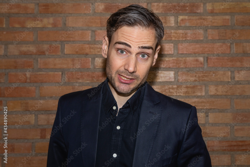 An influencer, artist and musician, speaks to the camera in one of his videos for social networks, while explaining his artistic career in a backstage area, with a reddish brick background, Spain. An influencer, artist and musician, speaks to the camera in one of his videos for social networks, while explaining his artistic career in a backstage area, with a reddish brick background, Spain.