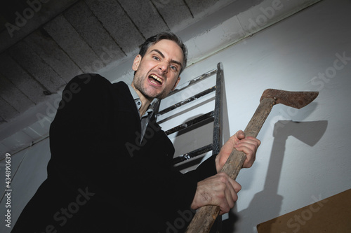 Φωτογραφία A psychopathic madman, young adult, threatens with an old and rusty ax in his hands, while he remains perched on a ladder, ready to attack with a violent expression