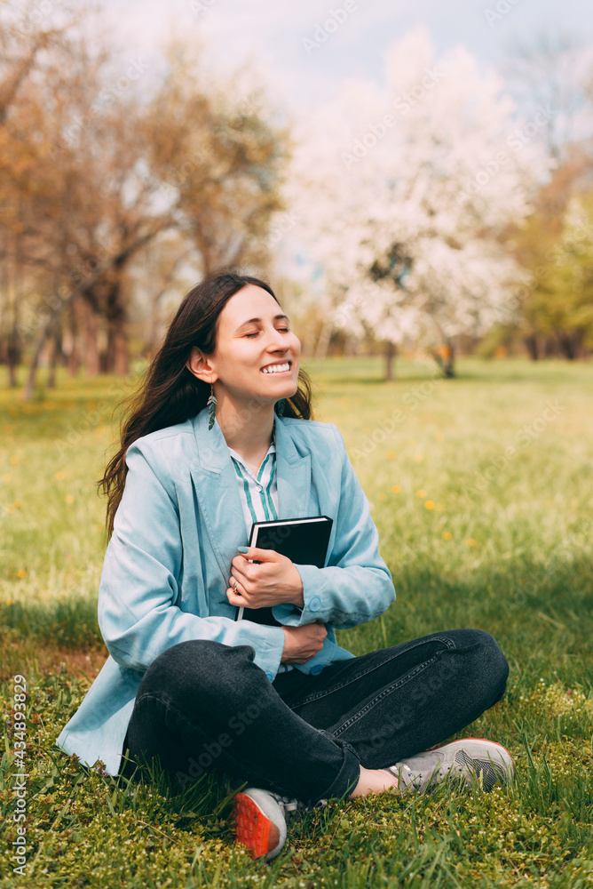 Photo of young woman in casual siting on grass in park and holding favorite book