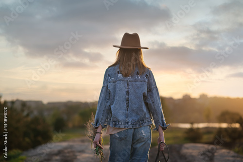A young girl in a hat walks down a country road at sunset.