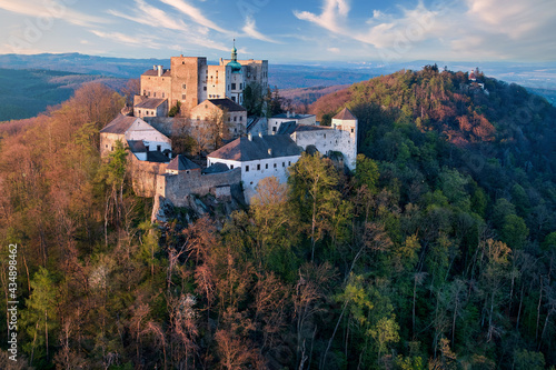 Buchlov Castle. Aerial view on monumental castle in Romanesque Gothic style, standing on a wooded hill against Saint Barbara’s Chapel on the hill in background. Spring, tourism hot spot. Czech castles photo