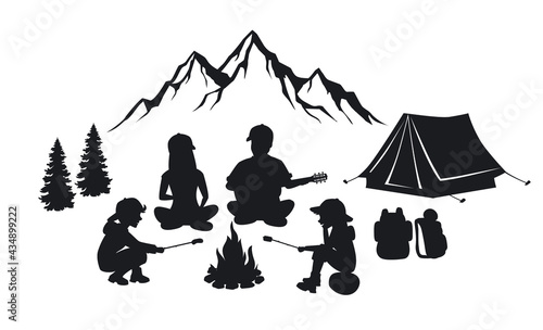 Family sit around campfire silhouette scene with mountains, tent and pine trees. People camping outdoor photo