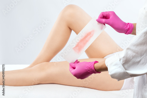 A beautician makes a depilation of a woman's legs in a beauty salon. Female aesthetic cosmetology.