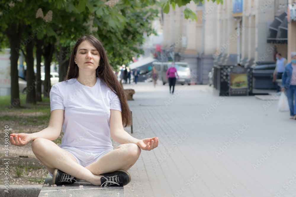 Beautiful brunette woman in white clothes meditates on the street in the city. Yoga and meditation, slowing down in the rhythm of modern life. Place for text. Beautiful brunette woman in white clothes meditates on the street in the city. Yoga and meditation, slowing down in the rhythm of modern life. Place for text.