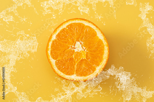 Splashing water on fresh orange on yellow background