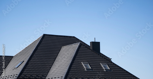 Brown corrugated metal profile roof installed on a modern house with a attic windows. The roof of corrugated sheet. Roofing of metal profile wavy shape. Modern roof made of metal. Metal roofing.