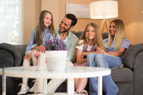 A shot of a four-member family with two adorable girls. They are sitting on the sofa and laughing.