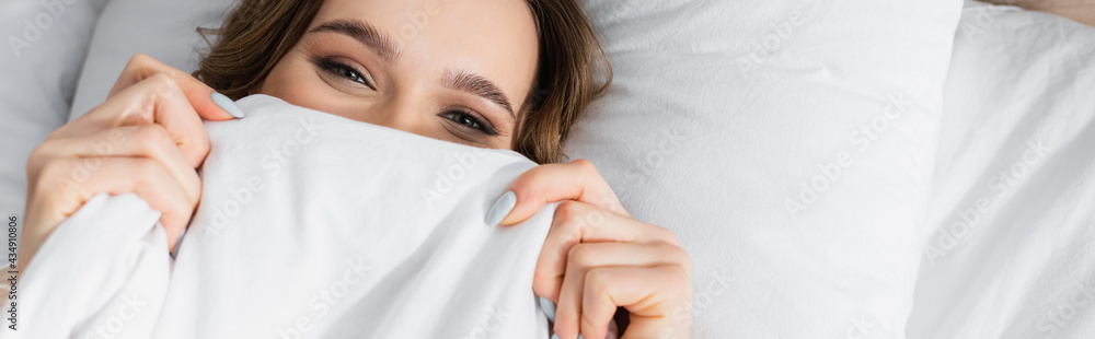 Top view of woman covering face with blanket and looking at camera, banner Top view of woman covering face with blanket and looking at camera, banner