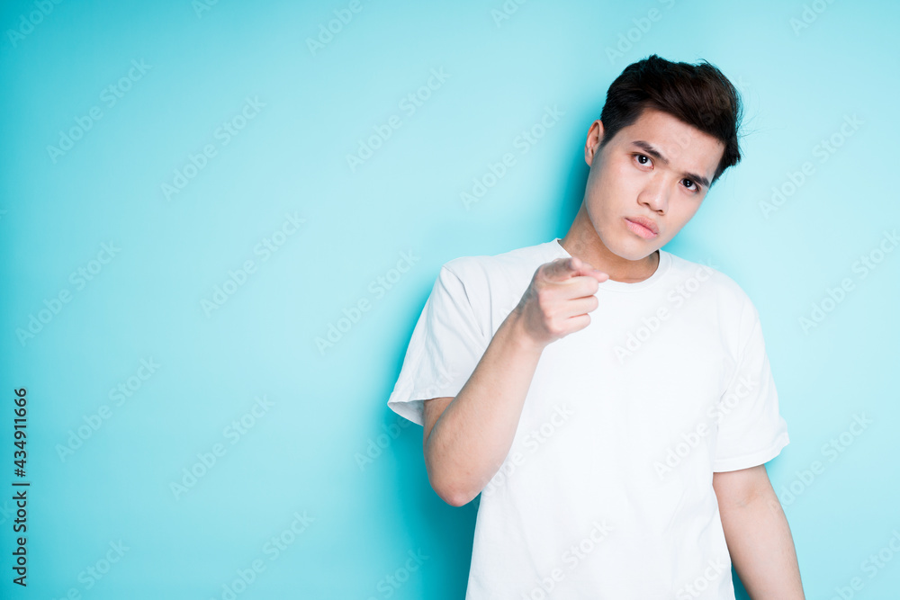 Cute serious asian guy stands on a blue background and shows his finger to the camera Cute serious asian guy stands on a blue background and shows his finger to the camera