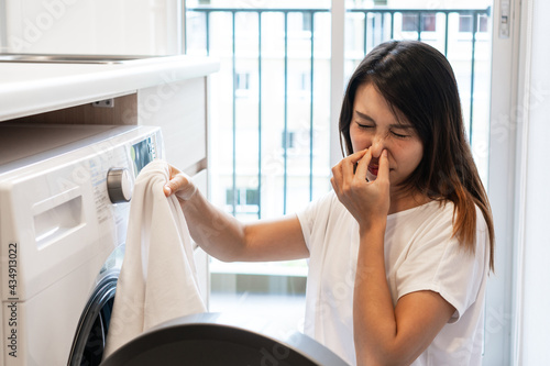Foto Young Asian woman looking at dirty smelly clothe out of washing machine in kitchen