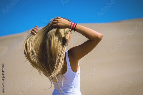 Chhica vestida de blanco peinandose en el desierto con ondas de arena mientras el viento sopla