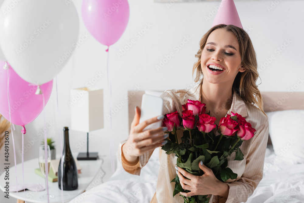 Smiling woman taking selfie on smartphone and holding roses during birthday celebration Smiling woman taking selfie on smartphone and holding roses during birthday celebration