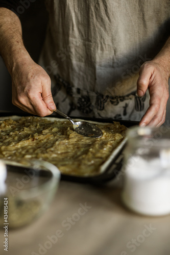 Male hands spreading onion pie filling on a baking sheet