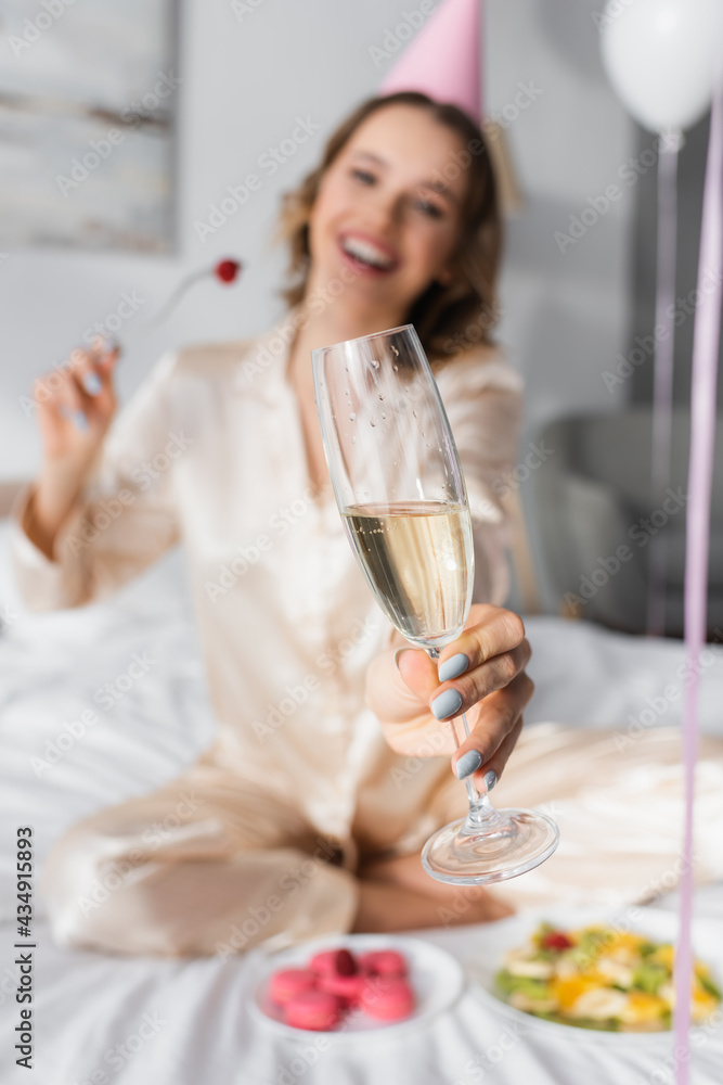 Blurred woman holding glass of champagne while celebrating birthday in bedroom