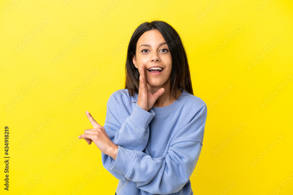 Young caucasian woman isolated on yellow background pointing to the side to present a product and whispering something Young caucasian woman isolated on yellow background pointing to the side to present a product and whispering something