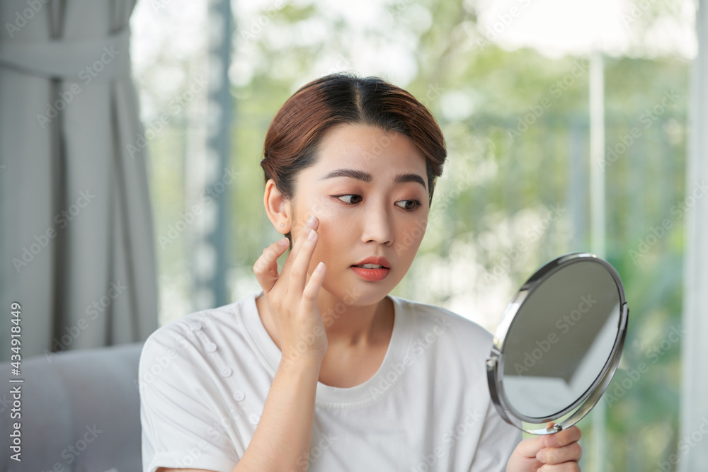 Woman examining her face in the mirror, problematic acne-prone skin concept Woman examining her face in the mirror, problematic acne-prone skin concept