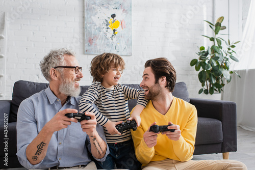 KYIV, UKRAINE - APRIL 12, 2021: Cheerful kid looking at father with joystick near grandfather photo