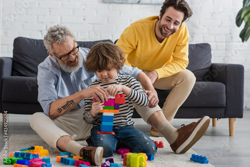 Kid stacking building blocks near grandfather and father in living room