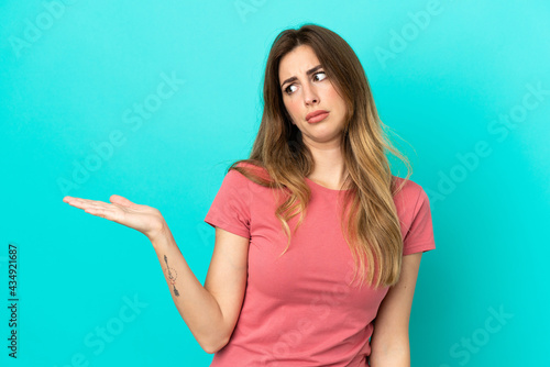 Young caucasian woman isolated on blue background holding copyspace with doubts