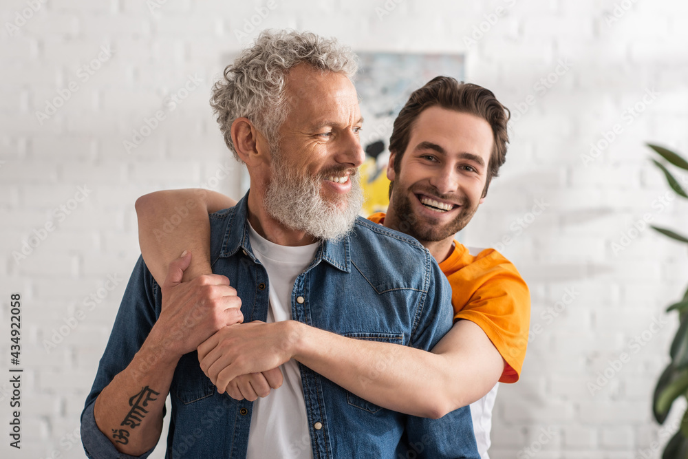 Smiling man hugging mature dad at home - obrazy, fototapety, plakaty 