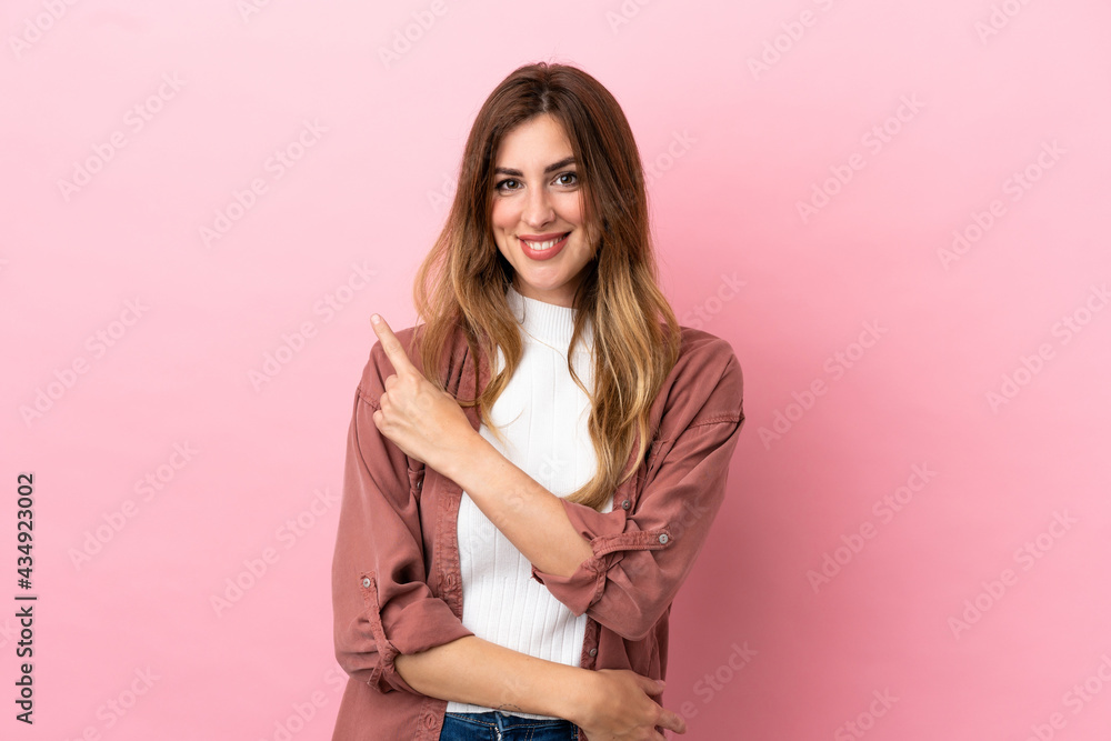Caucasian woman isolated on pink background pointing to the side to present a product Caucasian woman isolated on pink background pointing to the side to present a product