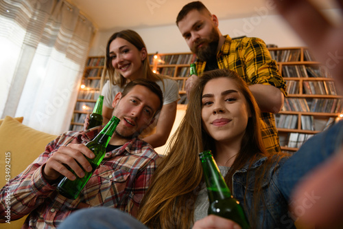 Friends hanging out together on a house party taking selfie with a smartphone and drinking beer