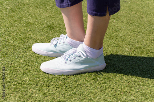 Close-up of women's legs in fashionable blue sneakers on a sunny summer day on a green lawn