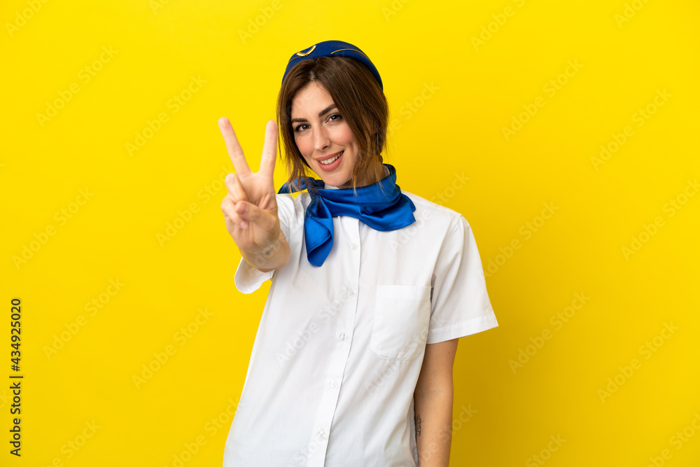 Airplane stewardess woman isolated on yellow background smiling and showing victory sign Airplane stewardess woman isolated on yellow background smiling and showing victory sign
