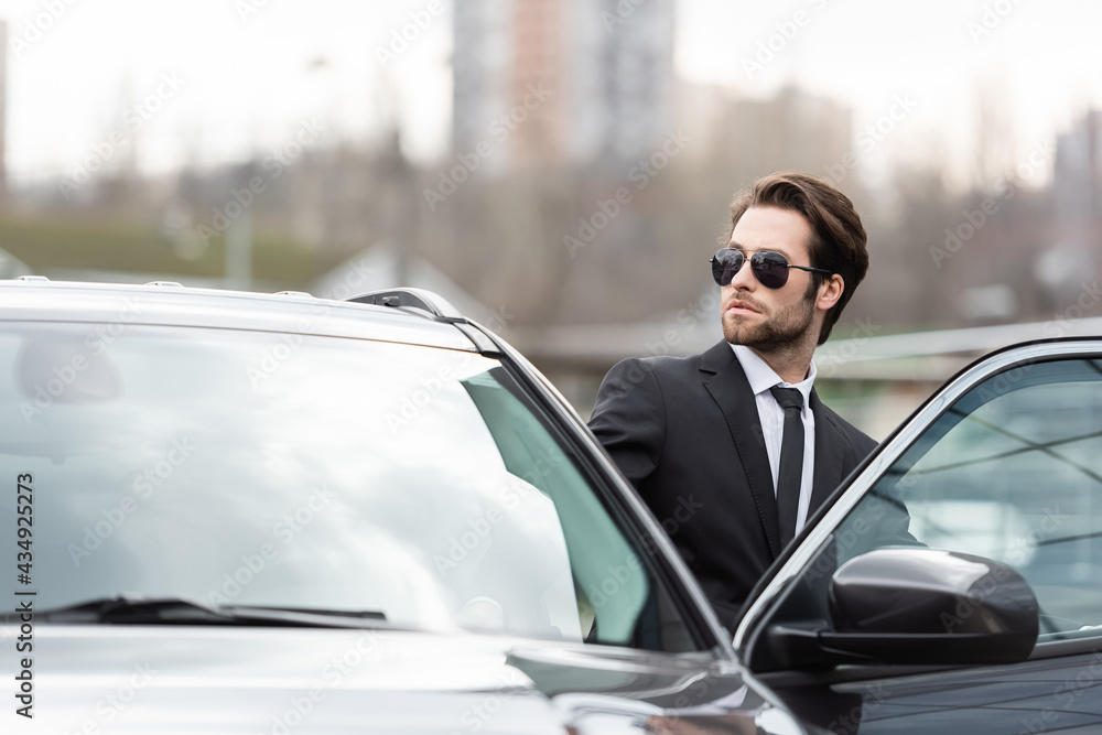 bearded businessman in suit and sunglasses sitting in modern car