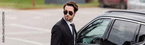 bearded bodyguard in suit and sunglasses with security earpiece near modern auto, banner © LIGHTFIELD STUDIOS