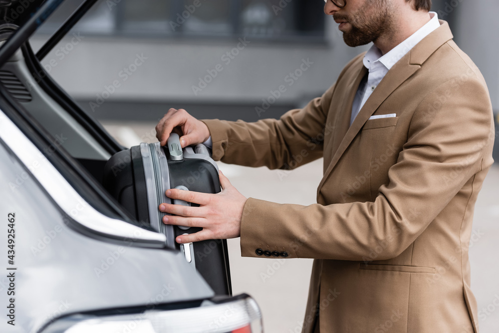 cropped view of bearded man in suit putting luggage in car trunk cropped view of bearded man in suit putting luggage in car trunk
